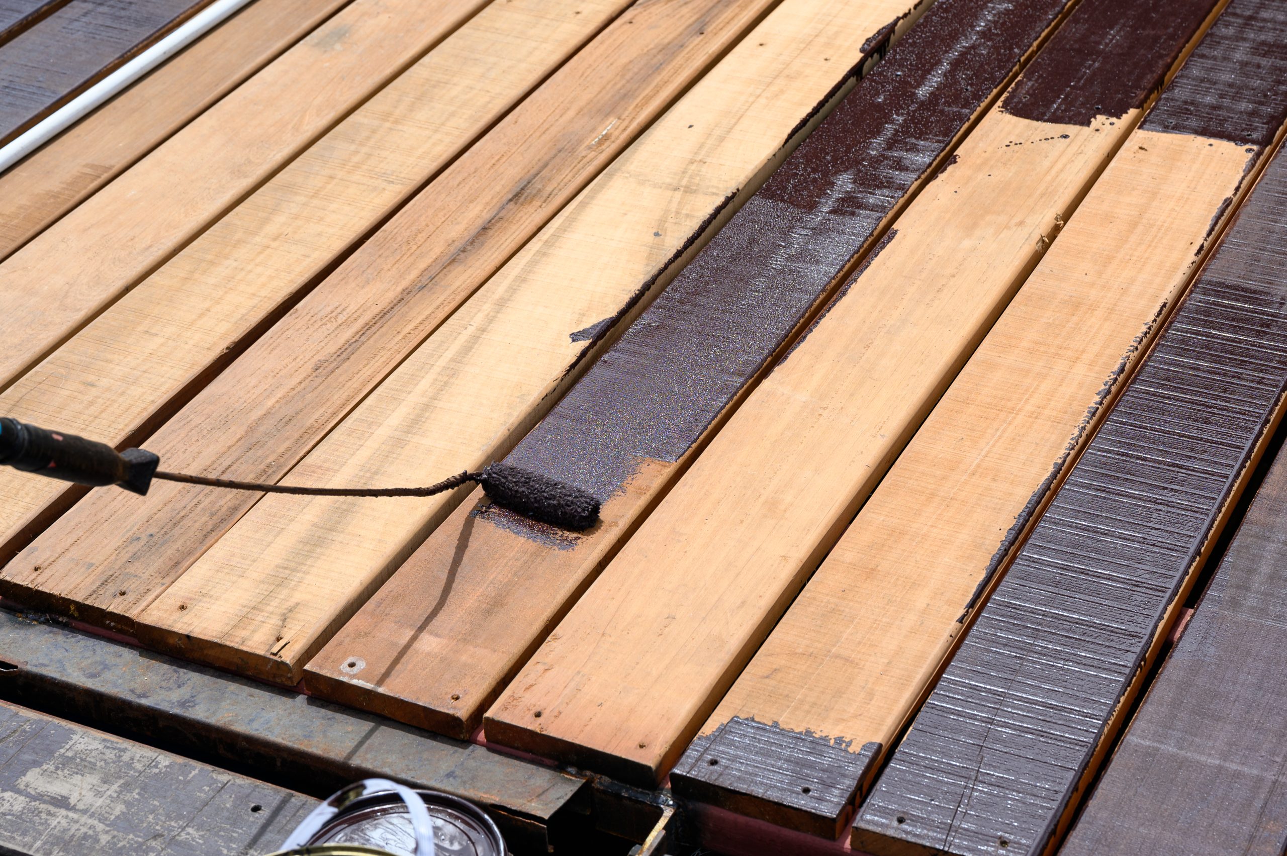 Professional applying brown stain to a wooden deck